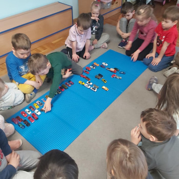 dziecko w zielonej bluzeczce bawi sie samochodziukami, inne dzieci patrzą.