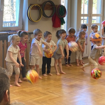 Dzieci stoja pod oknem i rzucaja piłki.