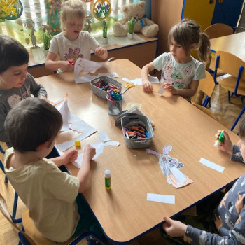Dzieci siedzą przy stole i kolorują na papierze postać królika