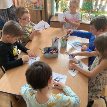 Dzieci siedzą przy stolikach i kolorują jaskółki. Następnie wydzierają je z papieru.
