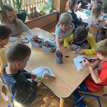 Dzieci siedzą przy stolikach i kolorują jaskółki. Następnie wydzierają je z papieru.